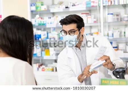 Middle eastern male pharmacist wearing protective hygienic mask to prevent infection selling medications to woman patient to prescription and making drug recommendations in modern pharmacy