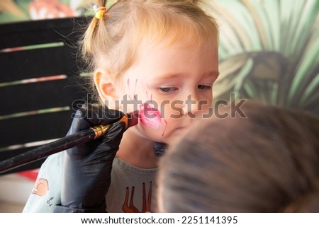 Make-up artist at the workplace to apply face painting to the model. Make-up artist at halloween party draw face painting on child's face.