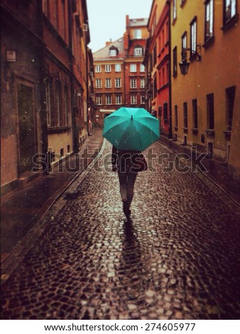 Woman with umbrella walking on the rain in old town of Warsaw, Poland. Vintage edited picture