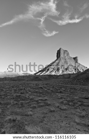 Black and white image of Parriott Mesa rising from the desert under a bird-like cloud formation near Moab, Utah