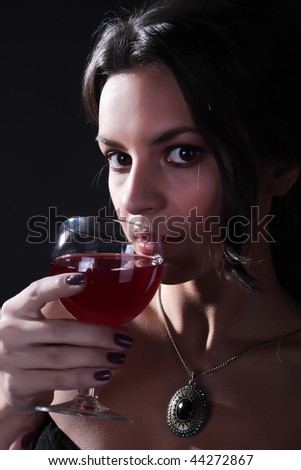The fine woman in an evening dress with a wine glass on a black background