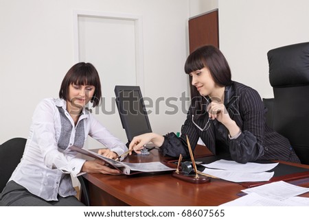 Two girls read documents at office behind a table