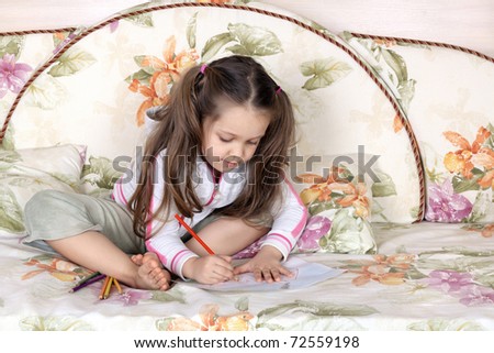 The little girl draws pencils sitting on a sofa