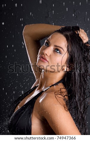 Portrait of the sexual young girl in a bathing suit in water splashes on a dark gray background