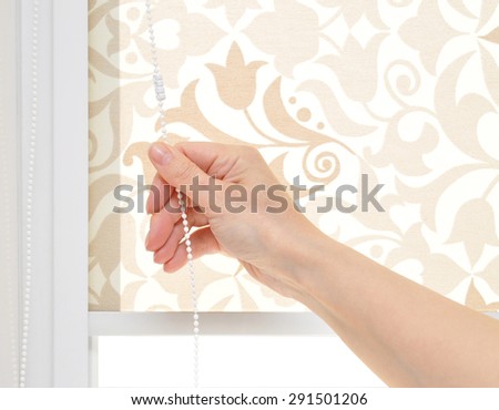 Young woman\'s hand opens the blinds on the window.