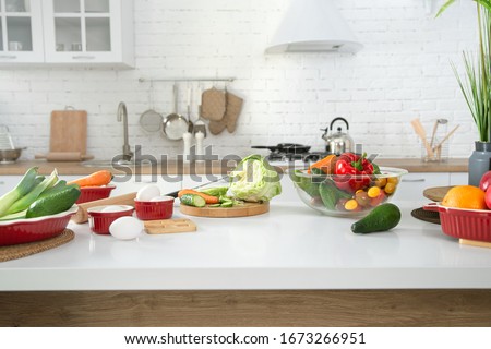 Modern stylish kitchen interior with vegetables and fruits on the table . Bright white kitchen with household items . The concept of a healthy lifestyle.