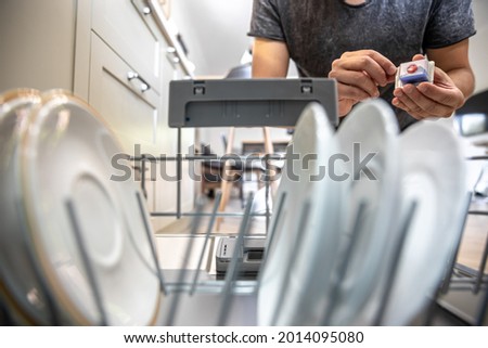 A man in front of an open dishwasher holds a tablet of dishwashing detergent in the dishwasher.