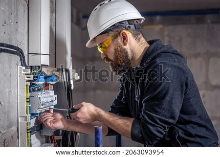 A male electrician works in a switchboard with an electrical connecting cable. Imagine de stoc © 