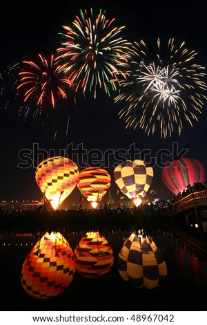 Night hot air balloons glow reflected in the water with beautiful fireworks in the sky