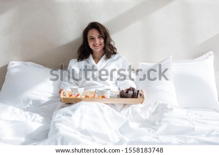 Young woman with a tray of food in bed wakes up smiling in the morning and enjoys life itself. Stock foto © 