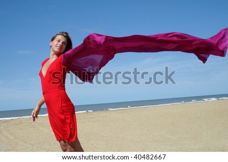 young woman in red dress on ocean beach with red scarf fluttering on wind