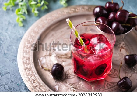 Cold sweet cherry non alcohol drink with ice on metal copper tray. Glass of red berries summer lemonade on gray-green table Stok fotoğraf © 