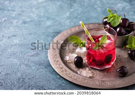 Cold sweet cherry non alcohol drink with ice on metal copper tray. Glass of red berries summer lemonade on gray-green table Stok fotoğraf © 