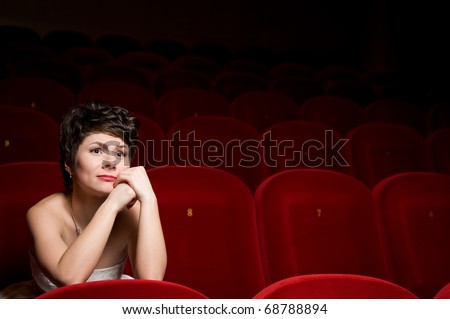 The beautiful girl in a white dress sits in a red armchair at a cinema alone