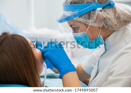 Female dentist curing teeth cavity in blue gloves and protective mask. Dentist caries treatment at dental clinic office. People, medicine, stomatology and health care concept Foto d'archivio © 