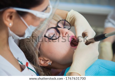 Closeup shot of dentist in protection mask working with tooth cavity and plague. Patient on stomatology chair repair aching teeth. Stomatologist and patient at clinic office. Toothcare concept Foto stock © 
