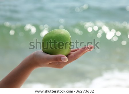 Woman`s hand holding a green apple on beautiful ocean background