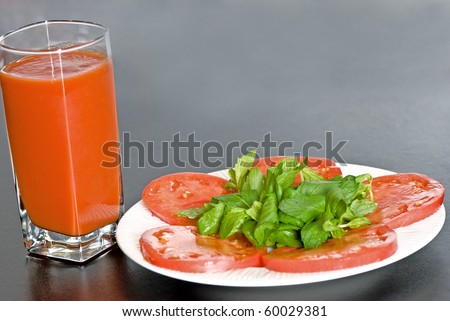 Tomato slices with green leaves and tomato juice in glass on black background