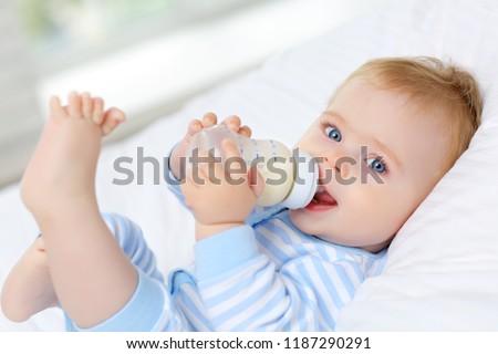 Charming blue-eyed baby 7 month old lies in bed and drinks milk from a bottle 商業照片 © 