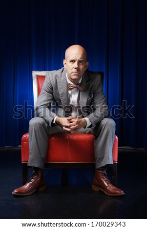 The bold man is sitting on the armchair