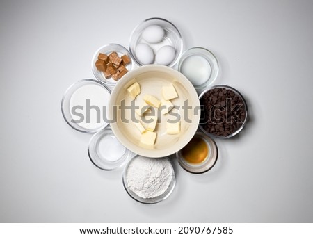 Top-down view of baking ingredients in Individual glass and ceramic baking bowls for brownies. Baking with chocolate, softened cut stick butter, eggs, flour, sugar chocolate chips, caramels, milk