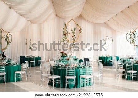 The decor of the wedding banquet hall with tables in emerald green, white drapery on the ceiling, gold geometric decorative elements. Stockfoto © 
