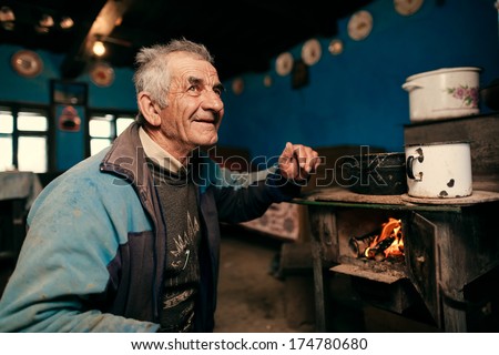 IEUD - OCTOBER 13 : Old man making fire in stove at farm on October 13, 2013 in Ieud , Maramures , Romania