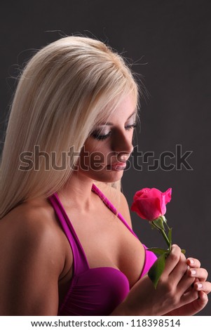 A young blond female woman in a pink top holding a red rose thing or missing the one who sent the rose on a black background.