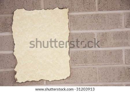 A blank piece of old paper burned on the edges against a brick wall in the horizontal format with copy space on the left side.
