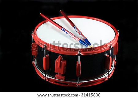 A red trimmed black snare drum and flag colored sticks isolated on black background in the horizontal format with copy space.