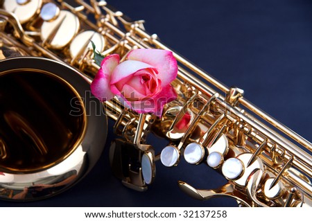 A gold brass saxophone with a pink rose isolated against a dark blue background in the horizontal format.