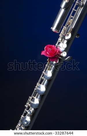 A silver bass flute with a red rose  isolated against a black background in the vertical format.