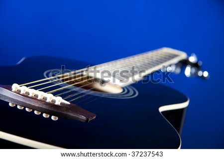 A black acoustic guitar isolated against a blue background in the horizontal format with copy space.