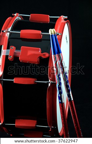 A red and black snare drum and multicolored sticks isolated on a black background in  the vertical format.