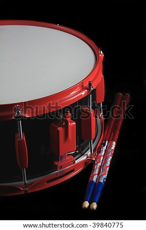 A red and black colored snare drum with flag colored sticks isolated against a black background in the vertical format.