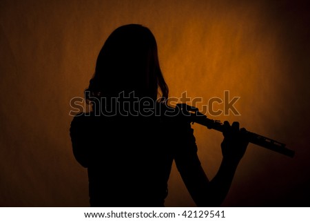 A teenager girl female flute performer player silhouette isolated against a spotlight gold background.