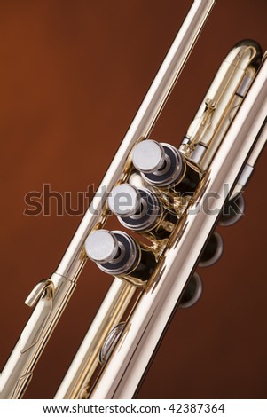 A gold brass trumpet music instrument against a spotlight gold background.
