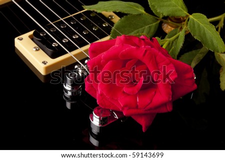 A red rose and stem on a black electric guitar in the horizontal format.