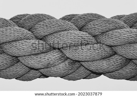 A black and white close up image of a thick industrial rope, with many rope lengths coiled together in a spiral.