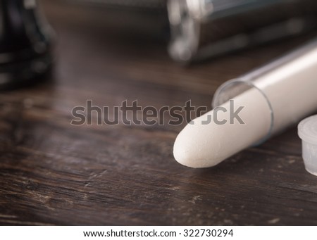 Styptic pencil in clear tube in bathroom setting on wooden counter with double edged razor and brush handle in the background