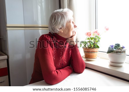 Old lonely woman sitting near the window at home. Concept of quarantine, coronavirus Covid-19. Danger for old people Foto d'archivio © 