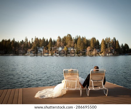 bride and groom relaxing on lawn chairs on the dock looking out to the lake