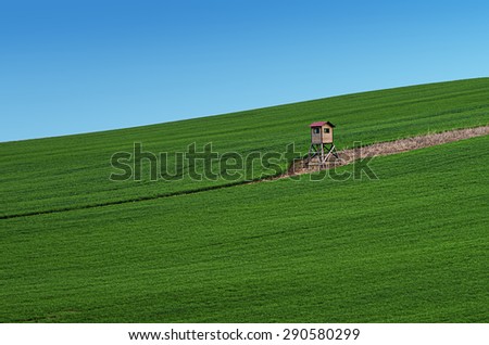 Rural landscape with green field, blue sky and wooden hunting shack , South Moravia, Czech Republic