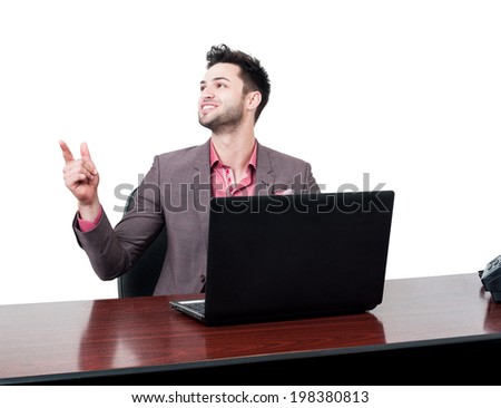 Handsome and smiling business man points with his finger in the air while sitting at his desk with a laptop