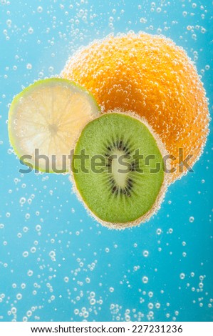 Fruits like orange, kiwi and lime in water with bubbles