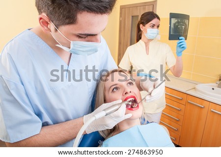 Beautiful woman patient in dentist office or cabinet getting her teeth checked by the young doctor
