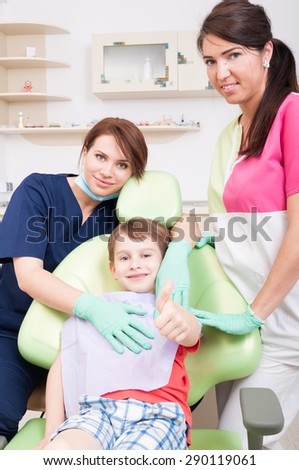 Happy child patient at dentist showing like with dental medical team arround