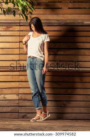 Young and beautiful female model wearing t-shirt and jeans on wooden background