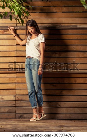 Female model wearing t-shirt and jeans outdoor in front of wooden fence