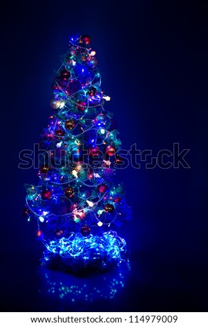 beautiful Christmas firtree with resplendent blue garland on dark blue background, blue light